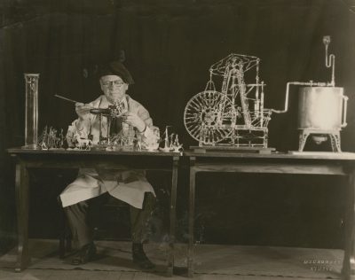 Black and white photograph of glassworker surrounded by his demonstration materials