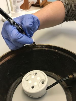 (Detail) Christy Cook, Associate Registrar, labels the lamp’s metal base with its number.