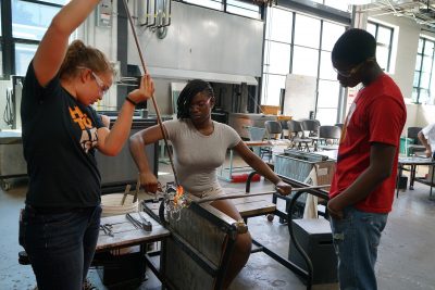 Teamwork is key when it comes to glassmaking. Nikki assists student Ja Mia Johnson as Trevelli Jones looks on.